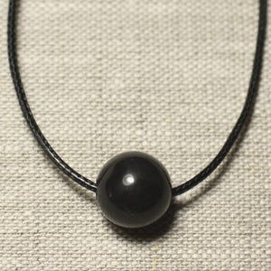 May include: A minimalist black necklace featuring a large, glossy, spherical bead suspended on a thin, black cord. The bead reflects light, creating a subtle shine. The necklace is displayed against a neutral, textured background.