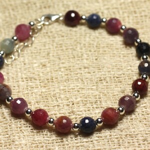 May include: A silver bracelet with a variety of gemstone beads in shades of pink, purple, blue, and black. The beads are faceted and have a polished finish.