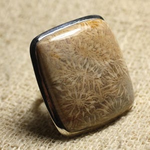 Peut inclure: Une bague en argent avec une pierre de corail fossilisé de forme carrée. La pierre est de couleur brun clair avec un motif blanc.