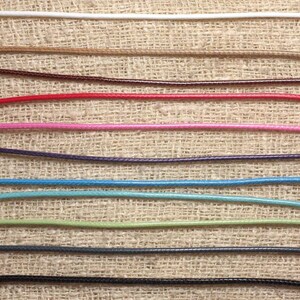 May include: A variety of colors of waxed cord, including white, brown, red, pink, purple, blue, green, gray, and black, are displayed on a burlap background.