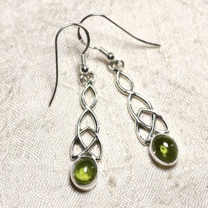 Peut inclure: Une paire de boucles d'oreilles argentées avec des nœuds celtiques et des pierres précieuses ovales vert olive. Les boucles d'oreilles ont une fermeture à crochet et un design détaillé et entrelacé. Les pierres sont serties.