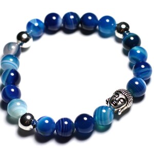 Puede incluir: Un brazalete de cuentas de ágata azul con un dije de Buda plateado. Las cuentas están graduadas en tamaño, con las cuentas más grandes en el centro del brazalete.