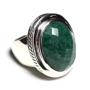 Puede incluir: Un anillo de plata con una gran piedra preciosa verde de forma ovalada engastada en un engaste de plata. El anillo tiene una banda texturizada y detallada.