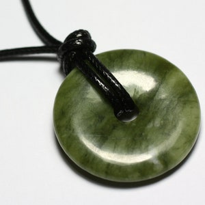 Könnte beinhalten: Ein grüner Jade-Anhänger in Donutform, der an einer schwarzen Schnur hängt.