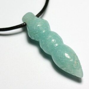 May include: A light blue, carved, gemstone pendant in the shape of a long, thin, pointed object. The pendant is on a black leather cord.