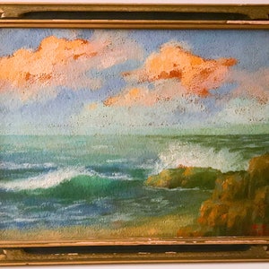 Pode incluir: Uma pintura emoldurada que retrata uma paisagem marítima com um oceano azul e verde, ondas brancas e espumosas quebrando contra costas rochosas, e um céu nublado com tons de laranja e rosa.
