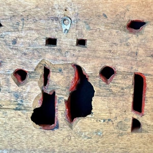 May include: A wooden board with multiple cutouts painted red. The board has a metal hook on the top.