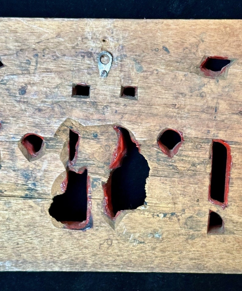 May include: A wooden board with multiple cutouts painted red. The board has a metal hook on the top.