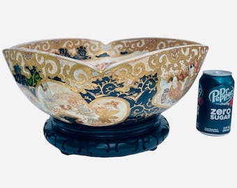 May include: An ornate, antique ceramic bowl with a black wooden base. The bowl features a gold rim and intricate designs in shades of blue, beige, and gold. A can of Dr. Pepper Zero Sugar is next to the bowl.