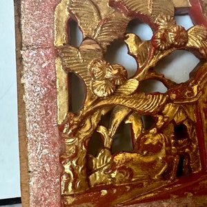 May include: A carved wooden panel with intricate floral and bird designs. The panel is painted in shades of red and gold, with the gold paint showing signs of wear and tear. The panel is likely from a traditional Chinese or Asian home.