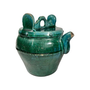 Op de afbeelding: Een groene theepot van keramiek met een uniek ontwerp. De theepot heeft een rond lichaam met een tuit en een handvat. Het handvat is gevormd als twee kleine oren. De theepot heeft een groene glazuur met een matte afwerking.