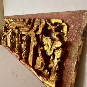 May include: A carved wooden panel with a red and gold finish. The panel depicts a scene with figures and a pagoda. The panel is intricately carved and has a distressed look.
