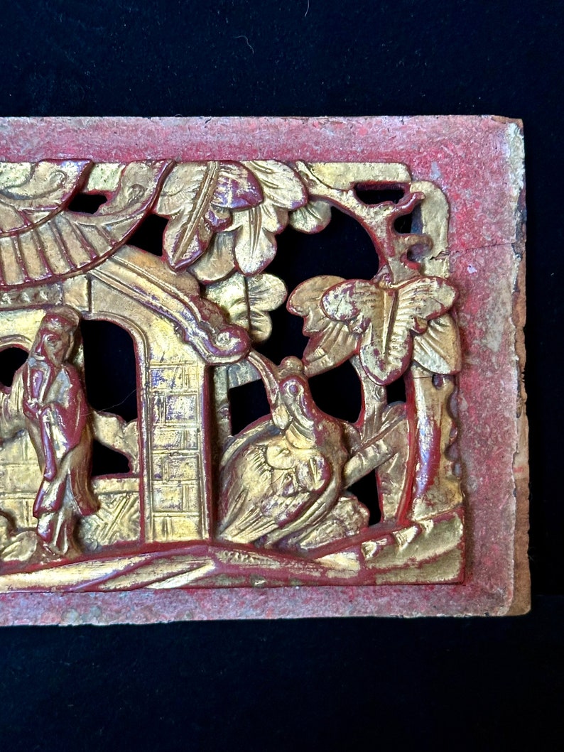 May include: A carved wooden panel with intricate details. The panel is painted in shades of red and gold, and features a scene of two figures in a garden setting. The figures are dressed in traditional Chinese clothing, and the garden is filled with flowers and trees.