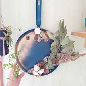 Peut inclure: Décoration murale faite à partir d'une poêle peinte en bleu. La poêle est ornée de feuilles séchées, de fleurs blanches et d'éléments en toile de jute. La poignée est bleu foncé.