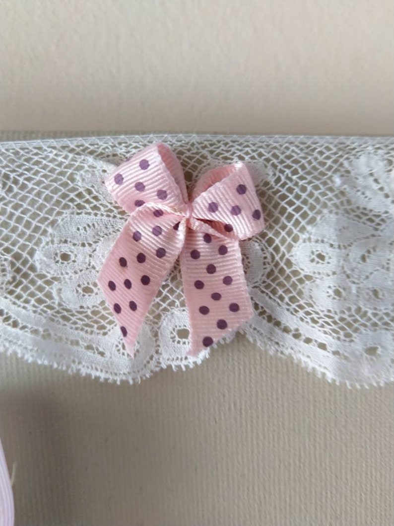 May include: A close-up of a pink polka-dot bow with a white lace trim. The bow is made of a satin ribbon and has dark purple polka dots. The lace trim is white and has a delicate, scalloped edge.