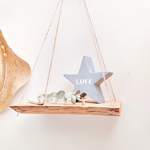 Op de afbeelding: Een houten plank die aan het plafond hangt met touw. De plank is versierd met een grijze ster waarop "LOVE" staat en een takje groen.