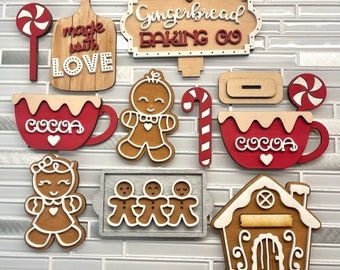 May include: A collection of wooden Christmas decorations, including gingerbread people, a gingerbread house, candy canes, and cocoa mugs. The decorations are in shades of red, white, and brown, with the words "made with LOVE" and "Gingerbread BAKING CO."