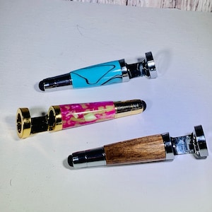 May include: Three stylus pens with different handle designs. One has a light blue and black swirl pattern, another has pink and yellow marbling, and the third has a wood grain pattern. All have silver metal accents.