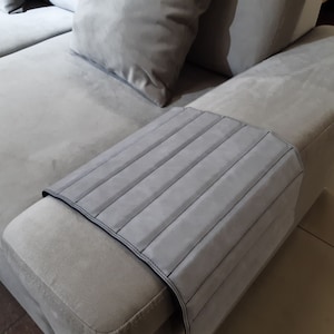 Puede incluir: Un sofá gris con una funda de reposabrazos gris. La funda del reposabrazos tiene un diseño acolchado con costuras verticales.