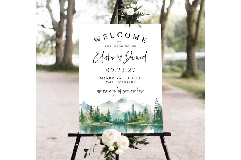 May include: A white wedding welcome sign with black text, including the names Elisha & Daniel, date 09.23.27, and location Manor Vail Lodge, Vail, Colorado. The bottom features a watercolor landscape of mountains and trees.