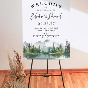 May include: A welcome sign for a wedding, displayed on a black easel. The sign reads "Welcome to the Wedding of Elisha & Daniel" with the date 09.23.27 and location Manor Vail Lodge, Vail, Colorado. A watercolor landscape is at the bottom.