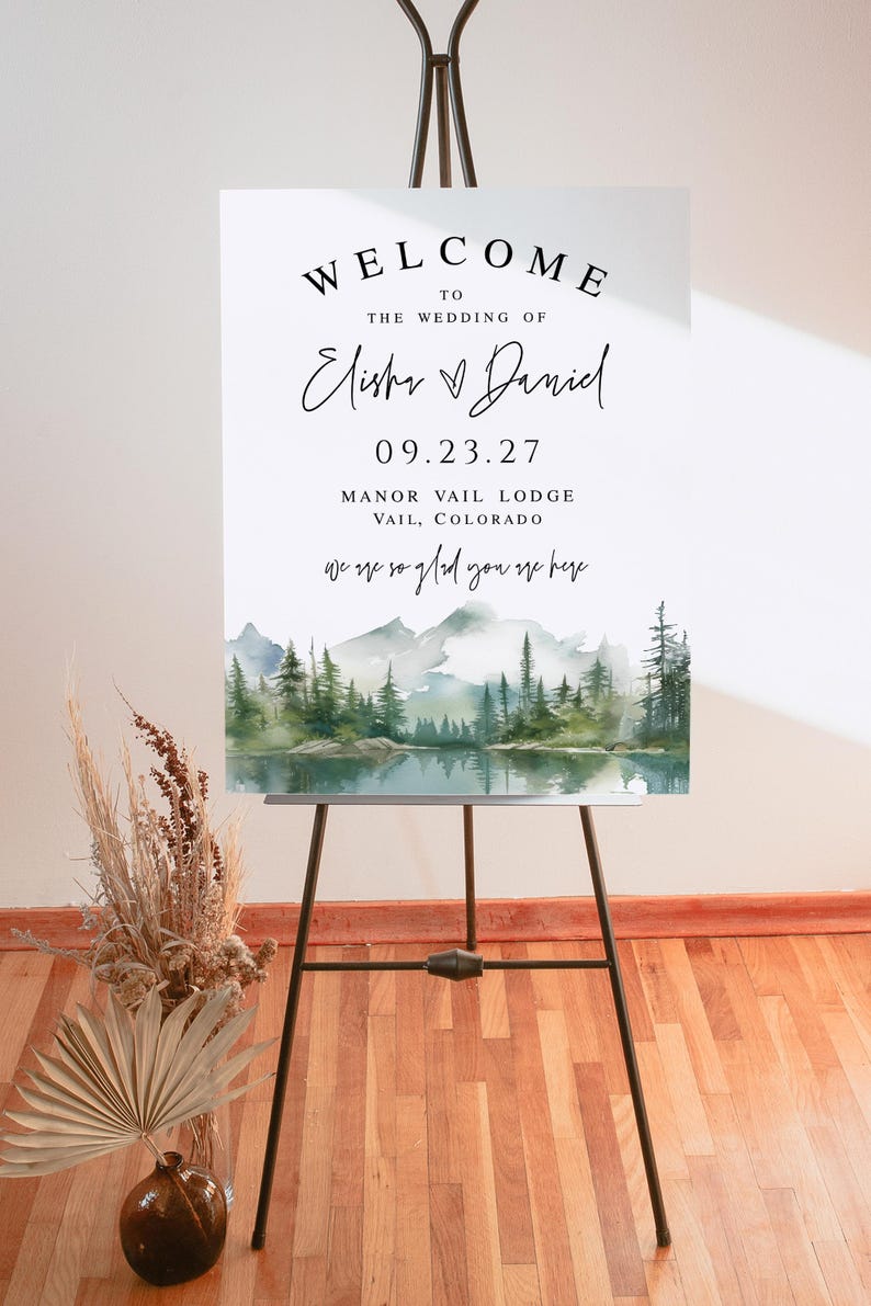 May include: A welcome sign for a wedding, displayed on a black easel. The sign reads "Welcome to the Wedding of Elisha & Daniel" with the date 09.23.27 and location Manor Vail Lodge, Vail, Colorado. A watercolor landscape is at the bottom.