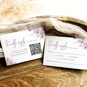 May include: Two white RSVP cards with a floral design and the text "Kindly reply by April 10th". One card has a QR code and the text "Please scan to RSVP or our wedding website: www.ourweddingday.com". The other card has a section for the guest's name, accepts, regrets, number of guests attending, and dietary requirements.