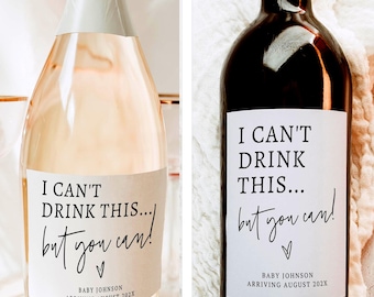 May include: Two bottles, one champagne and one wine, with custom labels. The labels read "I can't drink this... but you can!" with a heart and the text "Baby Johnson arriving August 202X".