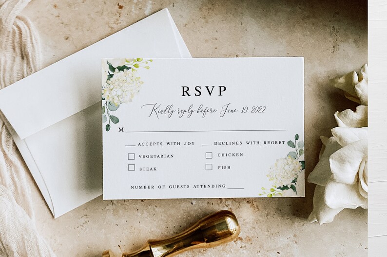 May include: A white RSVP card with a floral design featuring white hydrangeas and green leaves. The card has the text "RSVP" in black font and the text "Kindly reply before June 10, 2022" in cursive font. The card also includes a section for guests to indicate their meal preference and the number of guests attending.