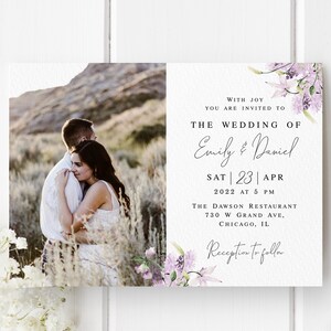 May include: Wedding invitation with a photo of a couple embracing in a field. The invitation features a floral design with purple flowers and the text "With joy you are invited to the wedding of Emily & Daniel Sat 23 Apr 2022 at 5 PM The Dawson Restaurant 730 W Grand Ave. Chicago, IL Reception to follow."