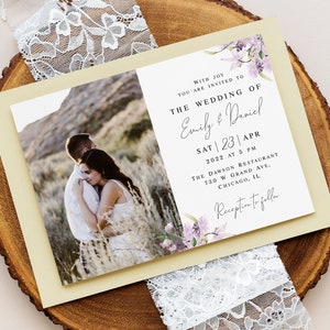 May include: Wedding invitation with a photo of a couple embracing in a field. The invitation is decorated with purple flowers and has the text "With joy you are invited to the wedding of Emily & Daniel Sat | 23 | Apr 2022 at 5 PM The Dawson Restaurant 730 W Grand Ave. Chicago, IL Reception to follow."