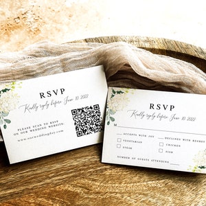 May include: Two white RSVP cards with floral designs. The top card has a QR code and the text "RSVP Kindly reply before June 10, 2022. Please scan to RSVP on our wedding website: www.ourweddingday.com". The bottom card has checkboxes for meal choices: Vegetarian, Steak, Chicken, Fish. It also has a line for the number of guests attending.