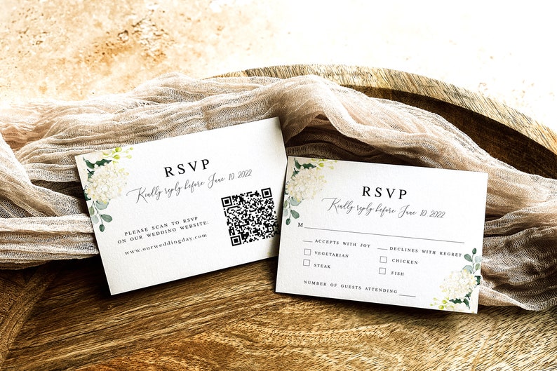 May include: Two white RSVP cards with floral designs. The top card has a QR code and the text "RSVP Kindly reply before June 10, 2022. Please scan to RSVP on our wedding website: www.ourweddingday.com". The bottom card has checkboxes for meal choices: Vegetarian, Steak, Chicken, Fish. It also has a line for the number of guests attending.