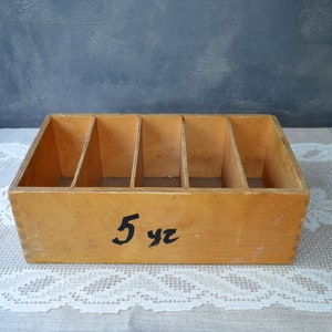 May include: A rectangular wooden organizer with five compartments. The box is made of light-colored wood and has black text that reads "5 yz" on the front. The organizer sits on a white lace tablecloth.