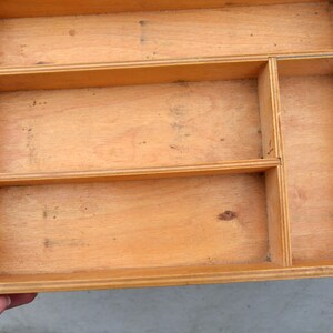 Op de afbeelding: Een lichtgekleurde houten organizerlade met meerdere compartimenten. De lade heeft een rechthoekige vorm met een natuurlijke houtnerf afwerking. Het heeft verschillende verdelers die verschillende opbergsecties cre&euml;ren en ronde handgreepuitsparingen.