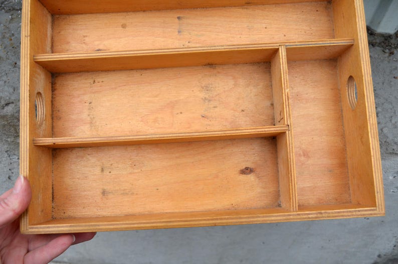 Op de afbeelding: Een lichtgekleurde houten organizerlade met meerdere compartimenten. De lade heeft een rechthoekige vorm met een natuurlijke houtnerf afwerking. Het heeft verschillende verdelers die verschillende opbergsecties cre&euml;ren en ronde handgreepuitsparingen.