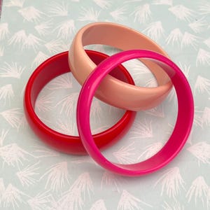 Pu&ograve; includere: Tre braccialetti colorati in rosso, rosa e pesca. I braccialetti sono realizzati in un materiale liscio e lucido e sono impilati. Questi braccialetti sono un accessorio classico, perfetto per aggiungere un tocco di colore a qualsiasi outfit.