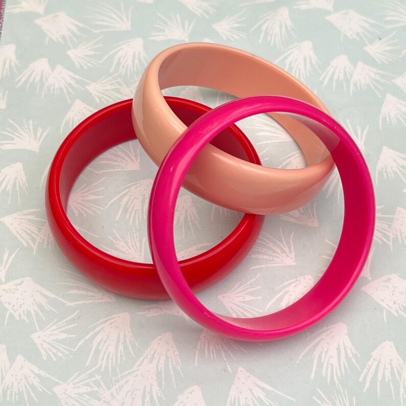 Pu&ograve; includere: Tre braccialetti colorati in rosso, rosa e pesca. I braccialetti sono realizzati in un materiale liscio e lucido e sono impilati. Questi braccialetti sono un accessorio classico, perfetto per aggiungere un tocco di colore a qualsiasi outfit.