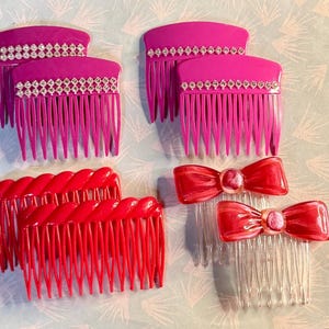May include: An assortment of hair combs in various styles and colors. There are several fuchsia combs with rhinestone accents, red twisted combs, and clear combs with red bow accents. The combs are arranged on a light blue patterned surface.