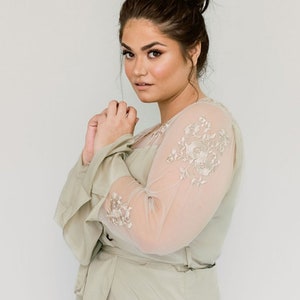 May include: A sage green robe with long sleeves and a delicate floral embroidery design. The robe has a wrap style closure and a sash tie.