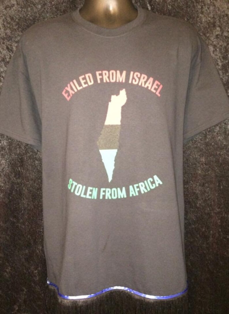 May include: Dark gray t-shirt with the text "EXILED FROM ISRAEL" in pink and "STOLEN FROM AFRICA" in green. A map of a country is in the center, with colors of black, white, and blue. The shirt has a blue and silver trim at the bottom.