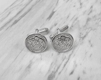 May include: A pair of silver cufflinks with a circular design featuring a detailed image of a bison. The cufflinks have a shiny finish and a classic, elegant design, perfect for formal wear or adding a touch of sophistication to any outfit.
