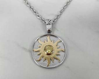 May include: A silver chain necklace with a round pendant featuring a gold sun with a yellow gemstone in the center.