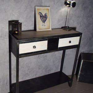 Peut inclure: Une console en métal noir avec deux tiroirs blancs et une étagère inférieure. La table a un plateau en bois et est décorée d'une estampe encadrée d'un coq.
