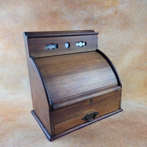 Peut inclure: Un bureau à rideau en bois vintage avec une finition marron foncé. Le bureau comporte un dessus roulant incurvé, un petit tiroir avec une poignée en métal et des découpes décoratives en haut. Un meuble classique.