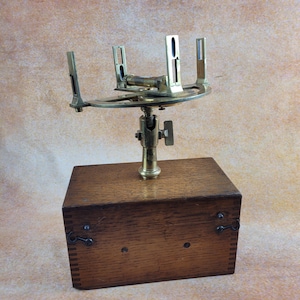 May include: A brass sextant with a wooden base. The sextant is a navigational instrument used to measure the angle between two objects, such as the sun and the horizon.