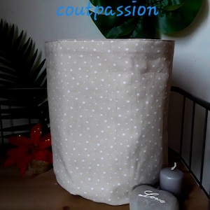 Peut inclure: Un panier de rangement en tissu beige à pois blancs. Le panier est posé sur une surface en bois avec un cœur en pierre grise sur lequel est inscrit "Love".