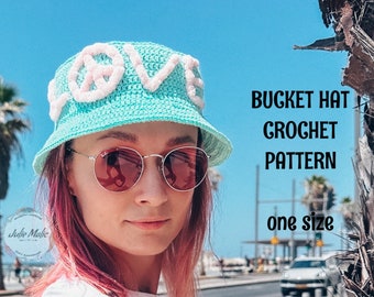 May include: A crochet bucket hat with a white "LOVE" design. The hat is light blue and has a white pom-pom on each letter. The hat is one size fits all. BUCKET HAT CROCHET PATTERN one size