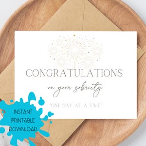 May include: A white card with the words "CONGRATULATIONS on your sobriety" and "ONE DAY AT A TIME" in elegant script. Gold fireworks graphic at the top. Includes a brown envelope and a blue splash with the words "INSTANT PRINTABLE DOWNLOAD".