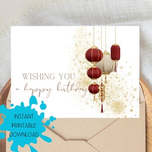 Könnte beinhalten: Geburtstagskarte mit weißem Hintergrund und goldenen Akzenten. Die Karte zeigt rote und weiße Laternen, die an goldenen Schnüren hängen. Der Text "WISHING YOU a happy birthday" ist in brauner Schrift geschrieben. Die Worte "INSTANT PRINTABLE DOWNLOAD" sind ebenfalls sichtbar.